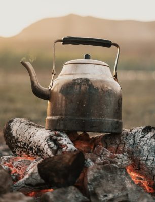 Close up Old kettle heated on a bonfire on a green mountain meadow. Epic travel in the mountains.